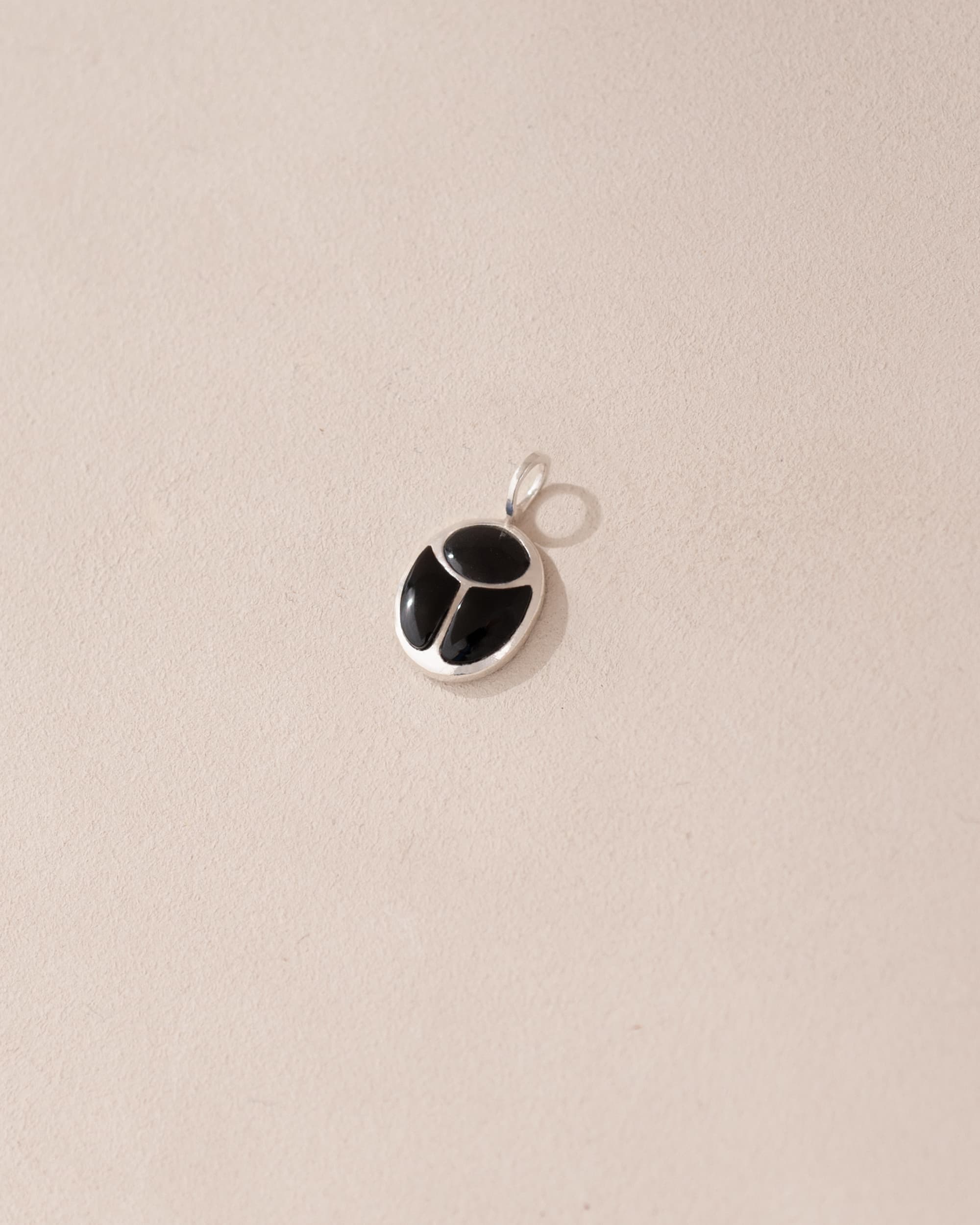A silver-colored charm with an onyx-like black center, displayed against a beige background.