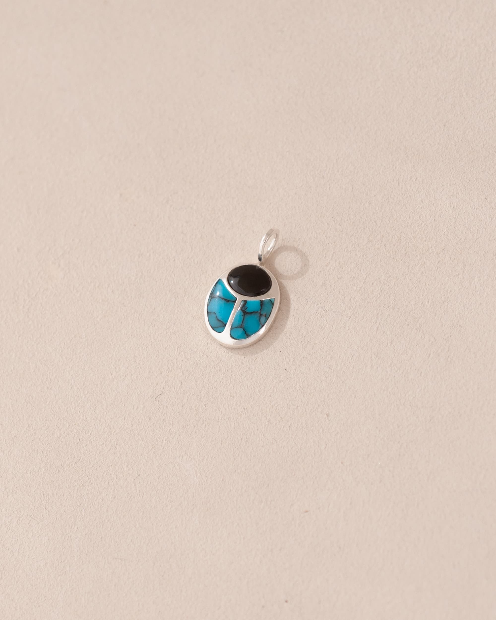 A small silver charm featuring a scarab design with onyx and turquoise inlays, displayed against a neutral background.