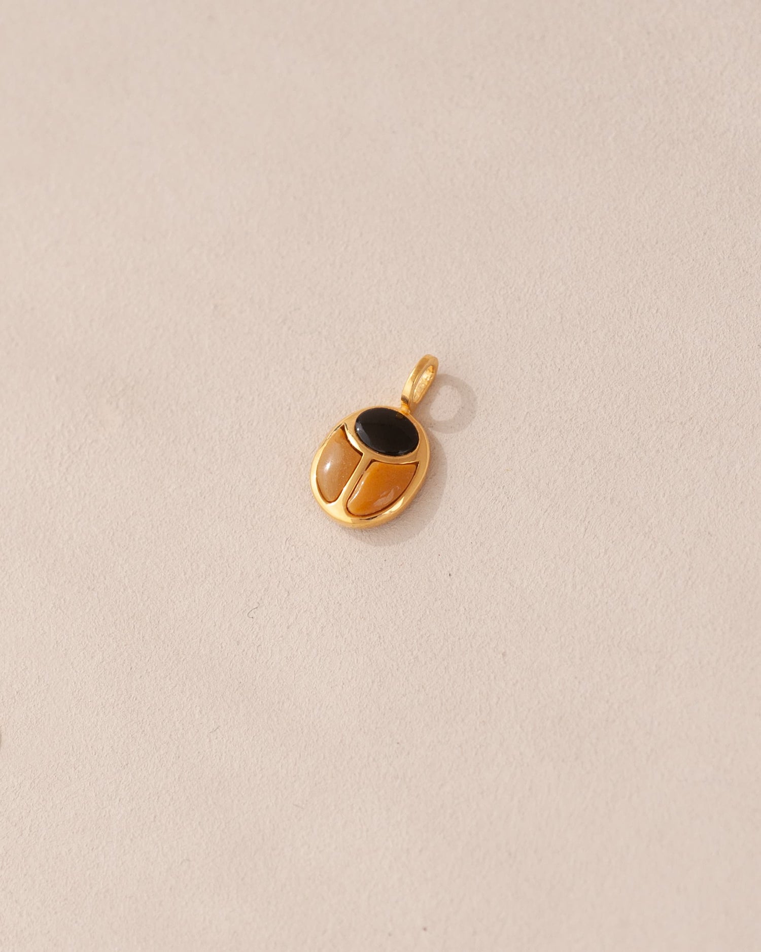 A gold charm featuring a scarab design with onyx and yellow opal inlays, displayed against a neutral background.