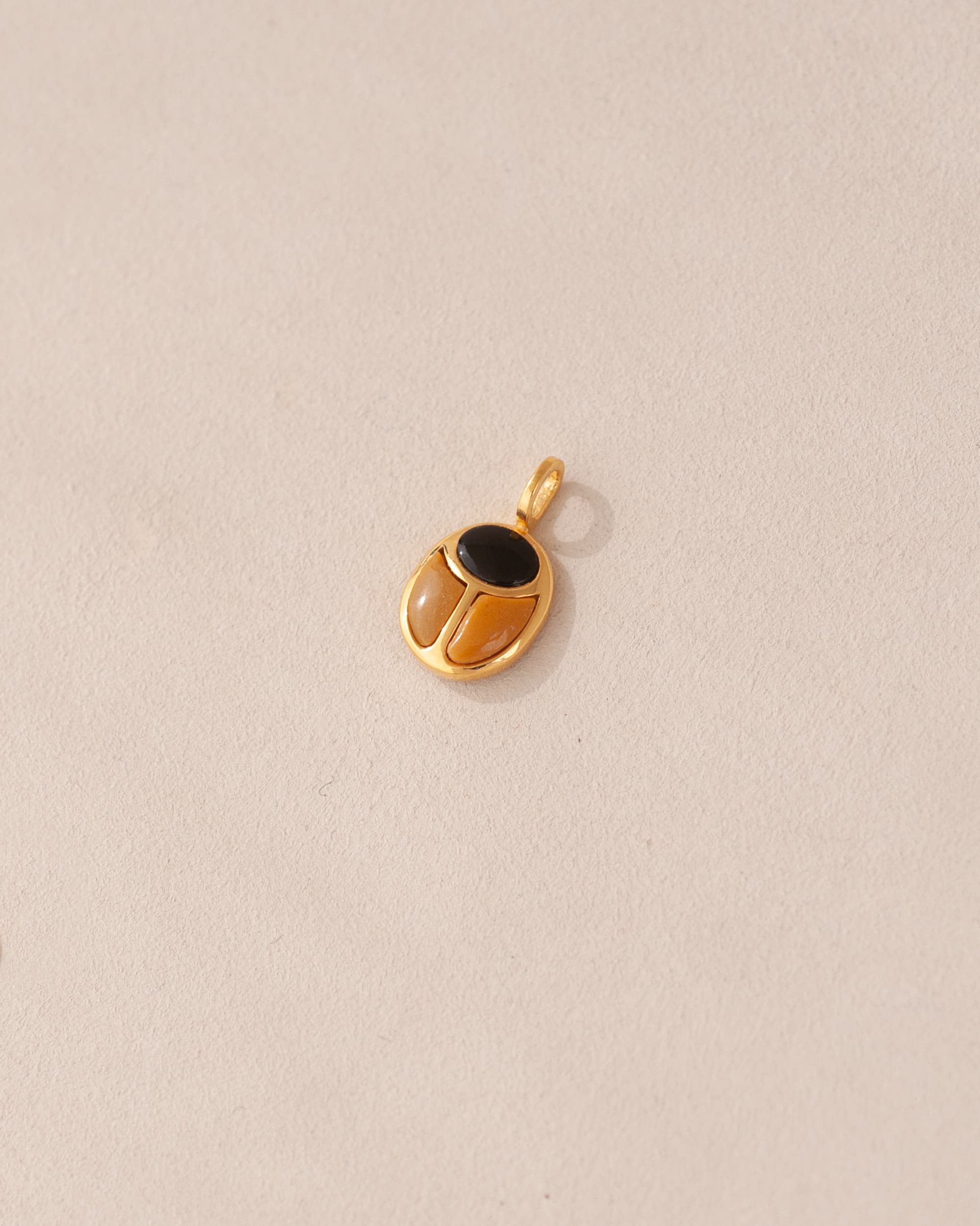 A gold charm featuring a scarab design with onyx and yellow opal inlays, displayed against a neutral background.