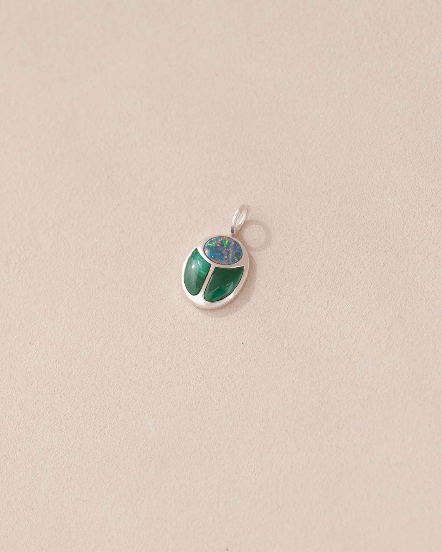 A silver charm with starry opal and malachite designs, against a beige background.