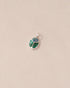 A silver charm with starry opal and malachite designs, against a beige background.