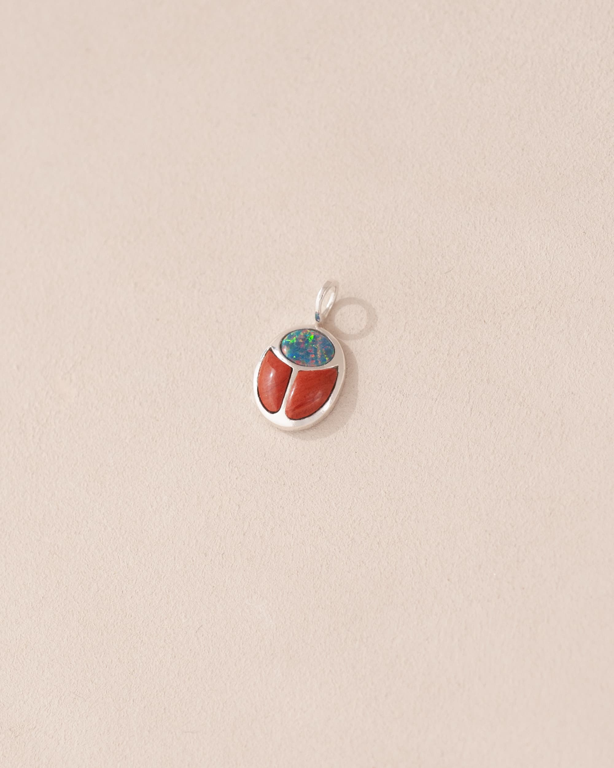 A silver charm featuring a starry opal and red jasper design, resembling a scarab amulet.
