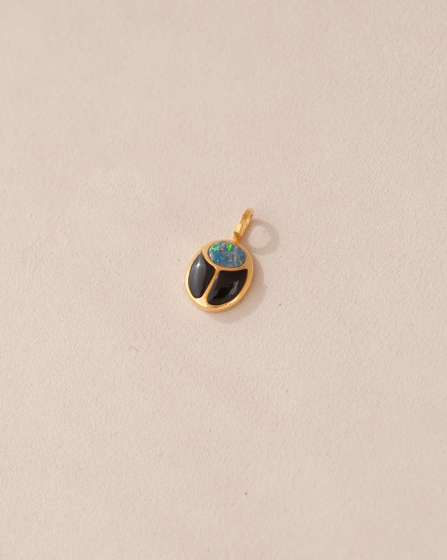 A 14K yellow gold charm featuring a starry opal and onyx design, resembling a scarab amulet.