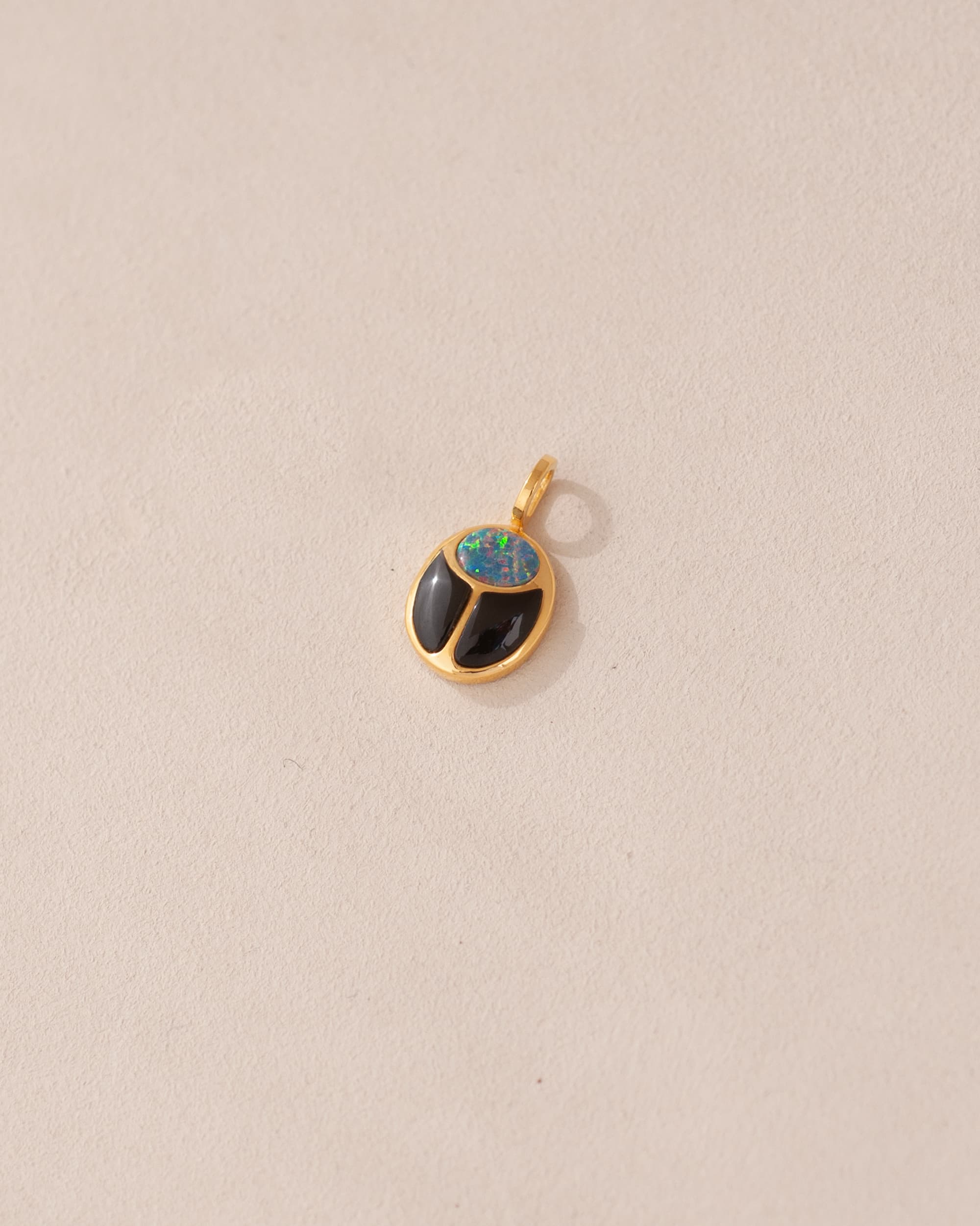 A 14K yellow gold charm featuring a starry opal and onyx design, resembling a scarab amulet.