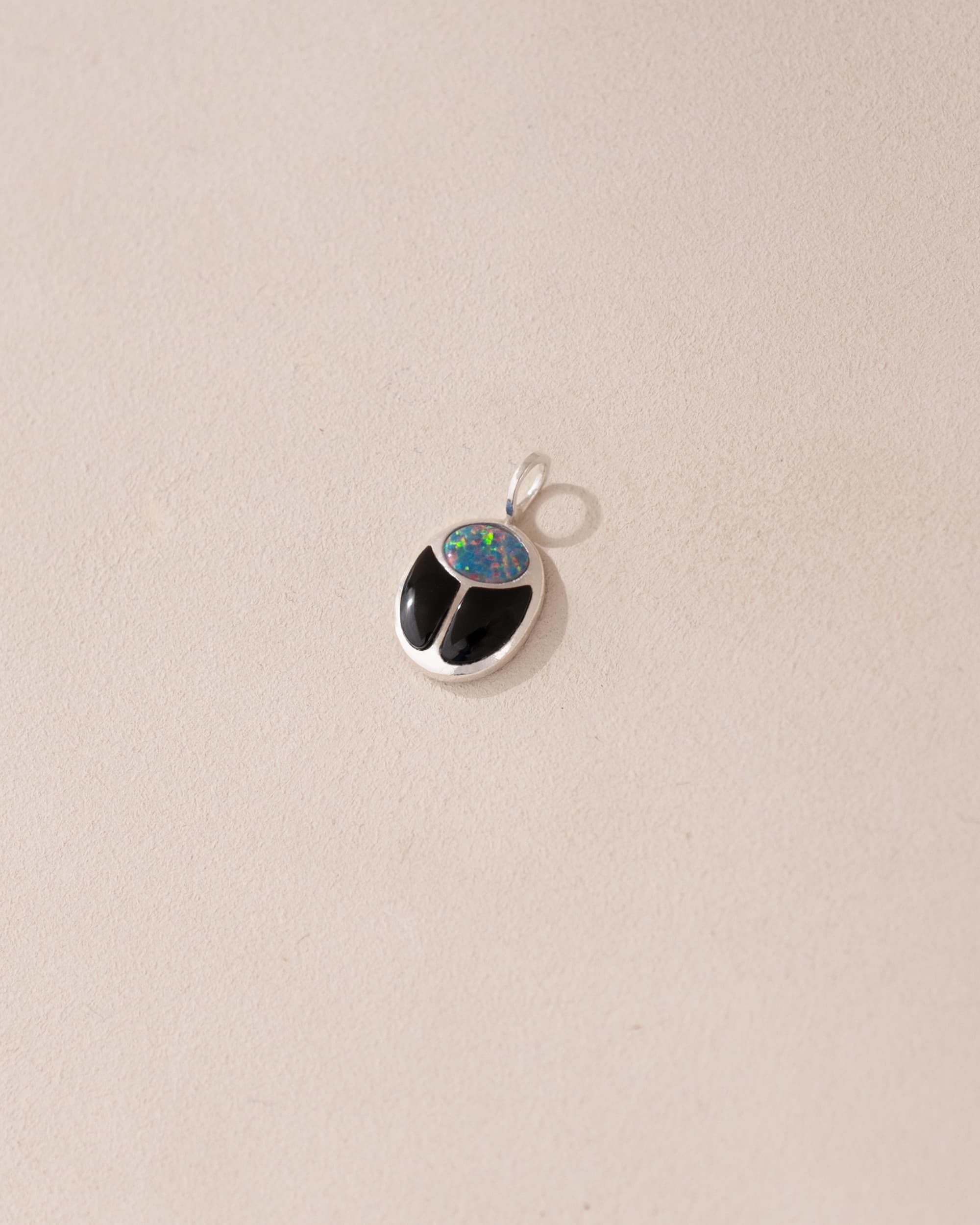 A small silver charm featuring a starry opal and onyx design, shaped like a scarab amulet.
