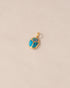 A gold charm featuring a scarab design with starry opal and turquoise inlay, placed against a beige background.