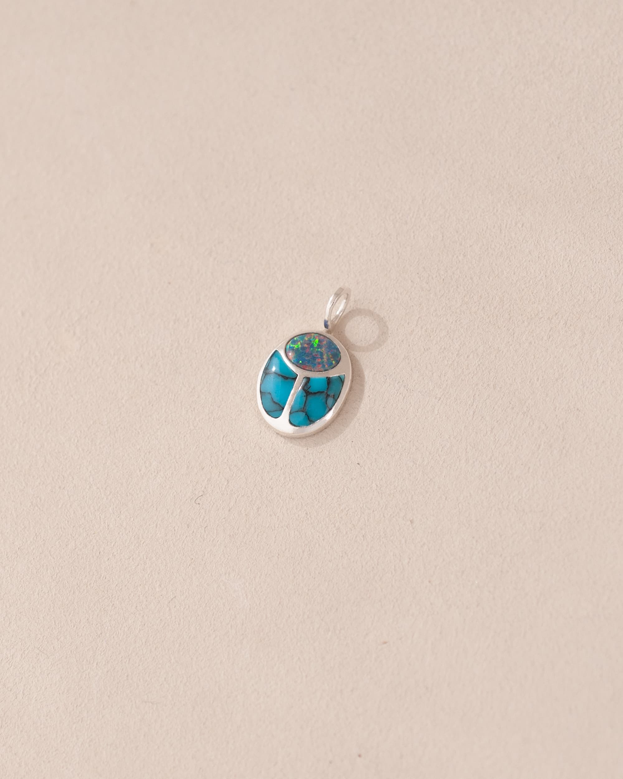 A silver charm featuring a starry opal and turquoise scarab design.