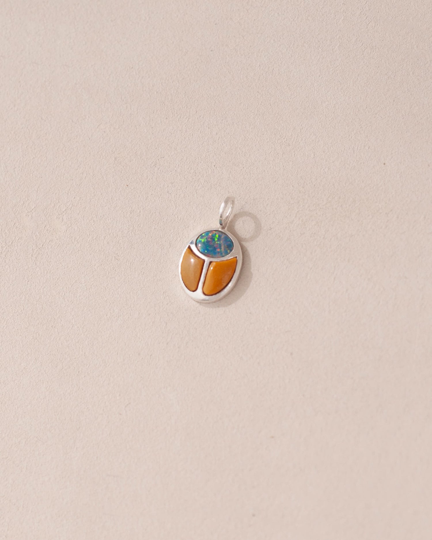 A silver charm featuring a starry opal and mookaite design, shaped like a scarab amulet, displayed against a neutral background.