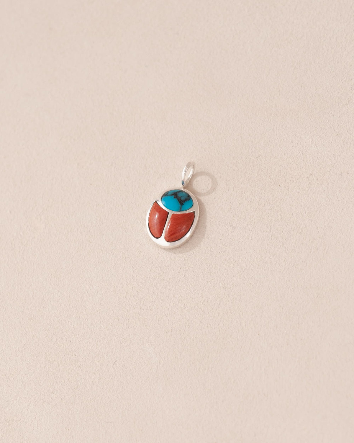 A small silver charm featuring a turquoise and red jasper design, shaped like a scarab amulet.