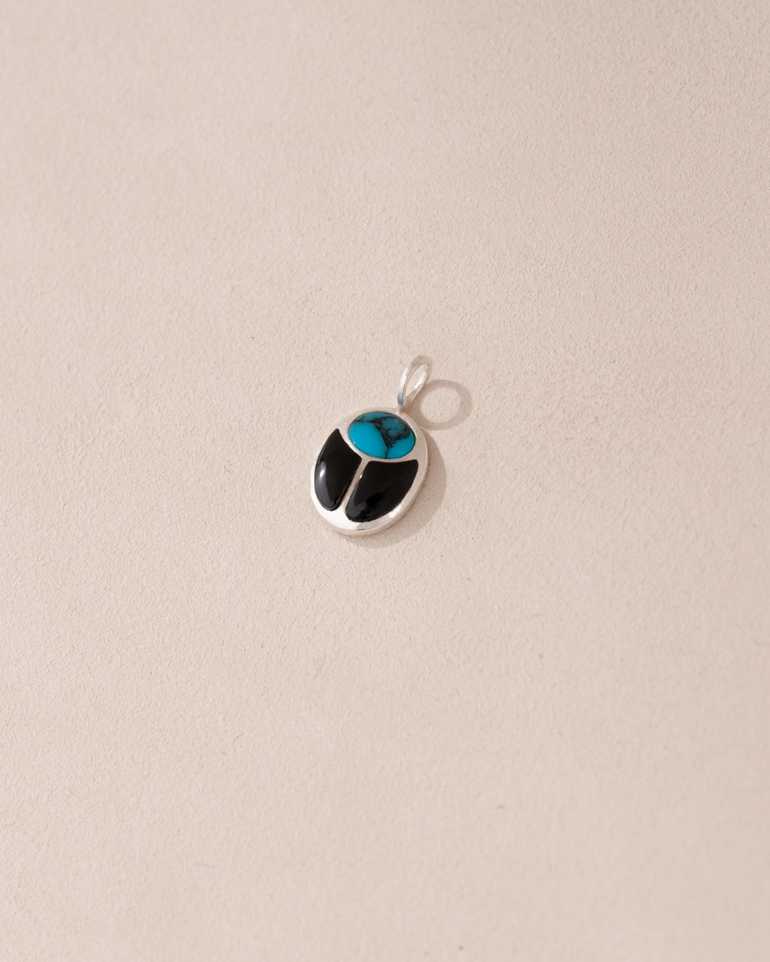 A small turquoise and onyx scarab charm in silver, displayed against a neutral background.