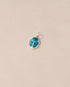 A small turquoise stone charm with a metallic setting, shaped like a scarab, displayed against a light background.
