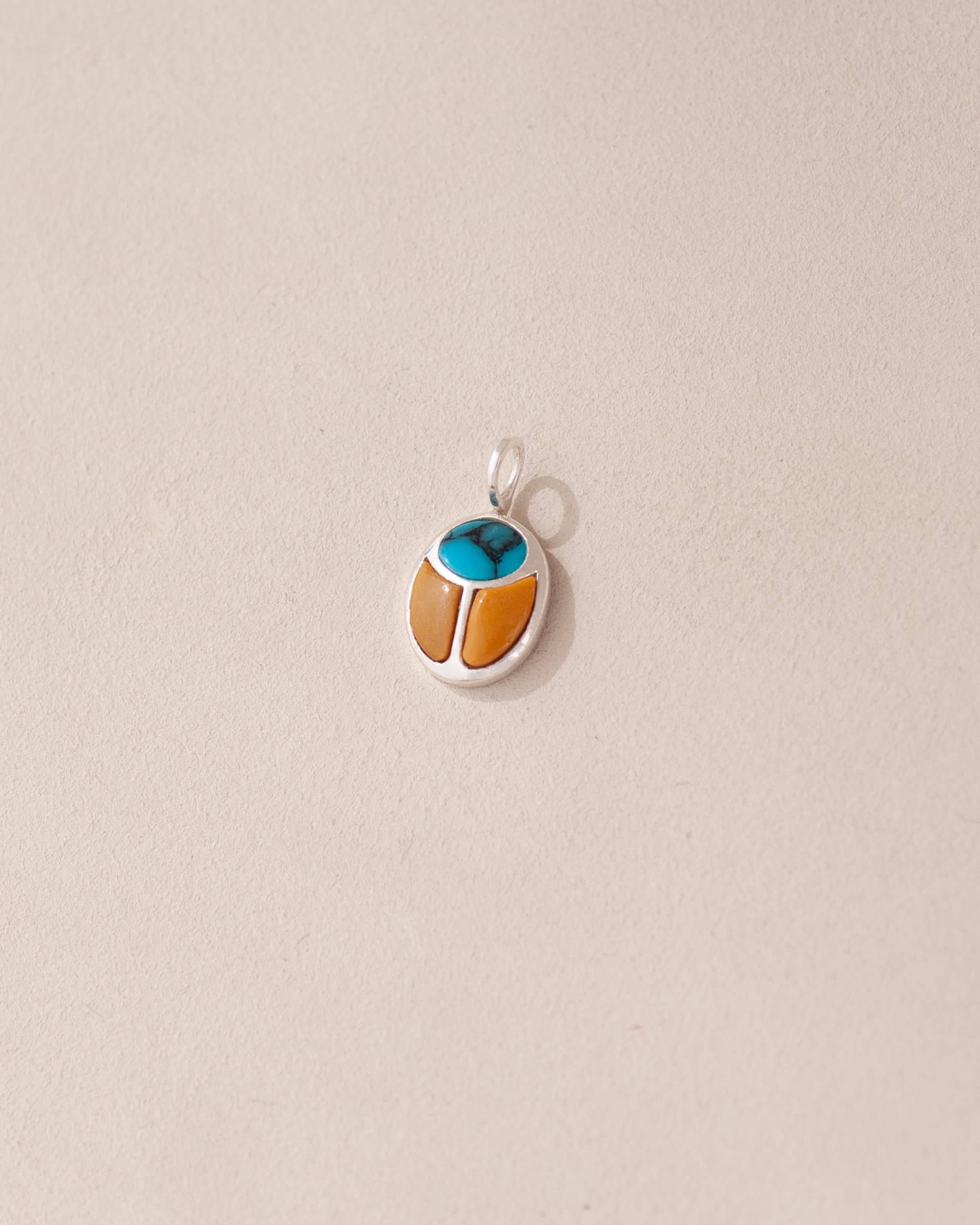 A silver charm featuring a turquoise and mookaite stone in the shape of a scarab amulet.