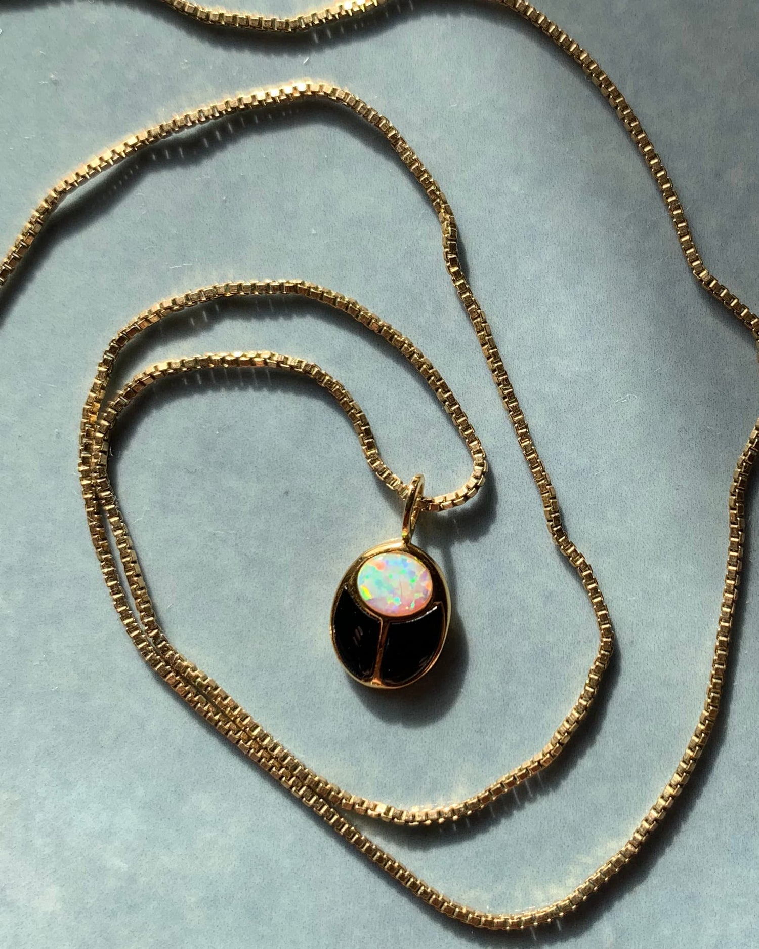 turquoise and opal charm in gold with gold hoops on a beige background