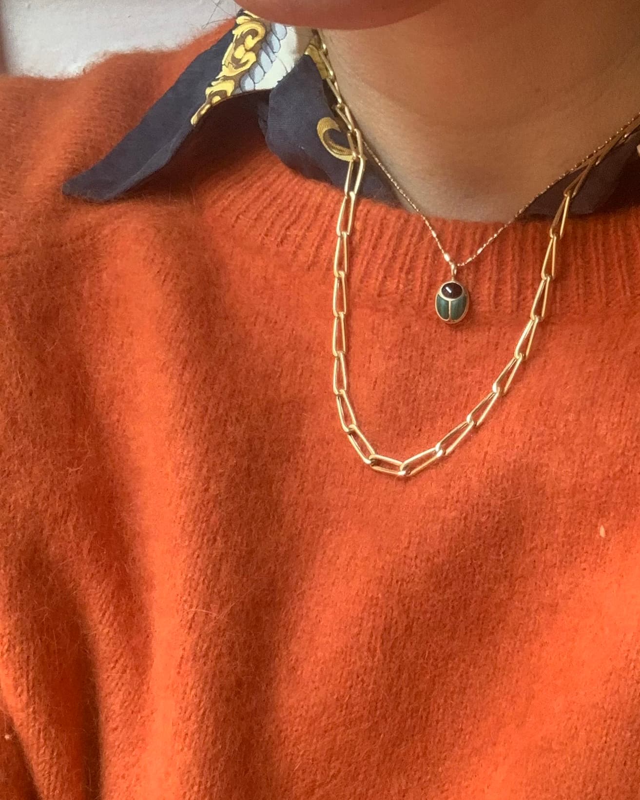 model wearing a scarab charm on a gold chain and an orange sweater