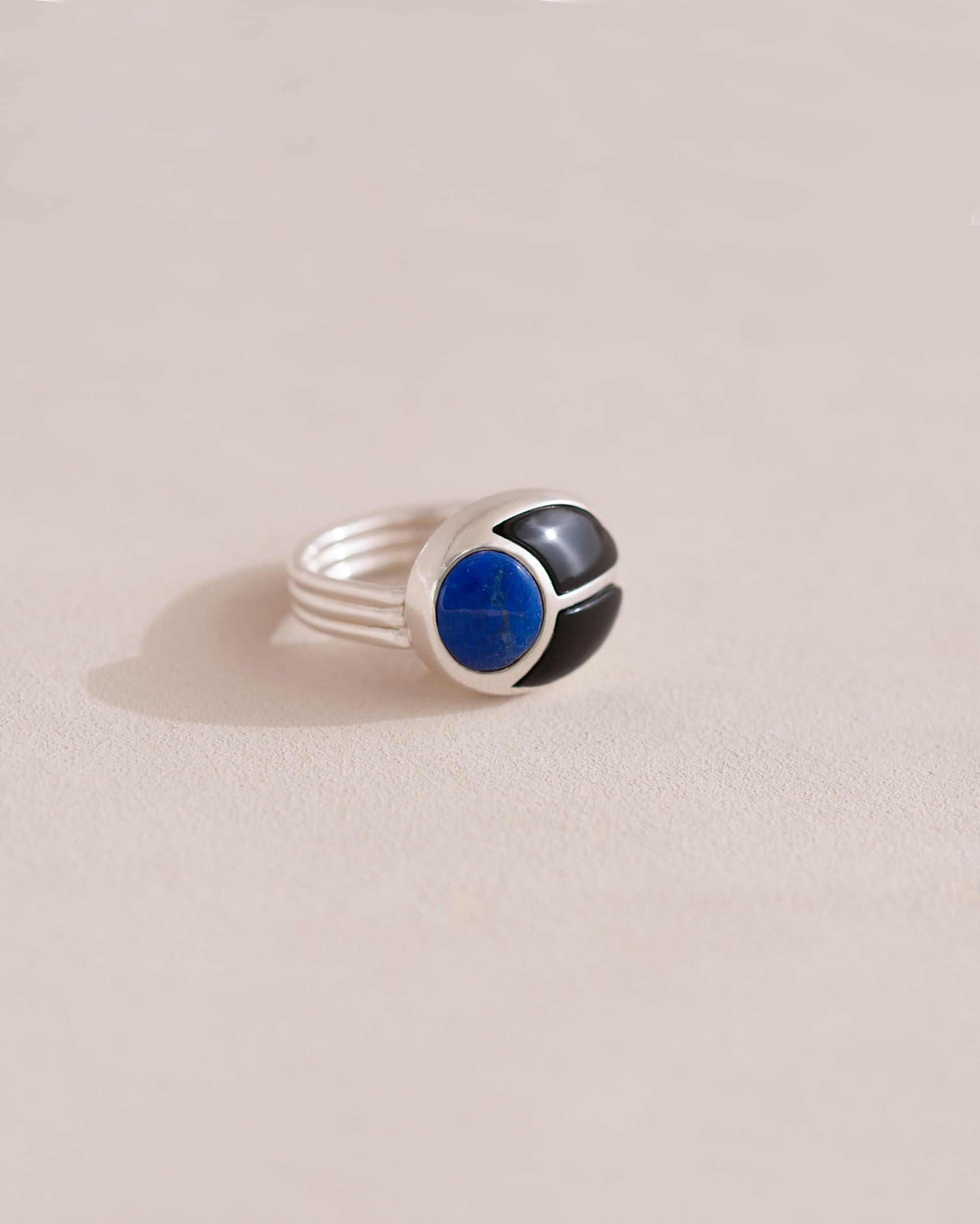 A gold ring featuring a central lapis lazuli stone flanked by onyx stones on either side, set against a neutral background.