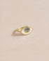 A gold ring with a labradorite stone in the shape of an eye, placed on a light background.