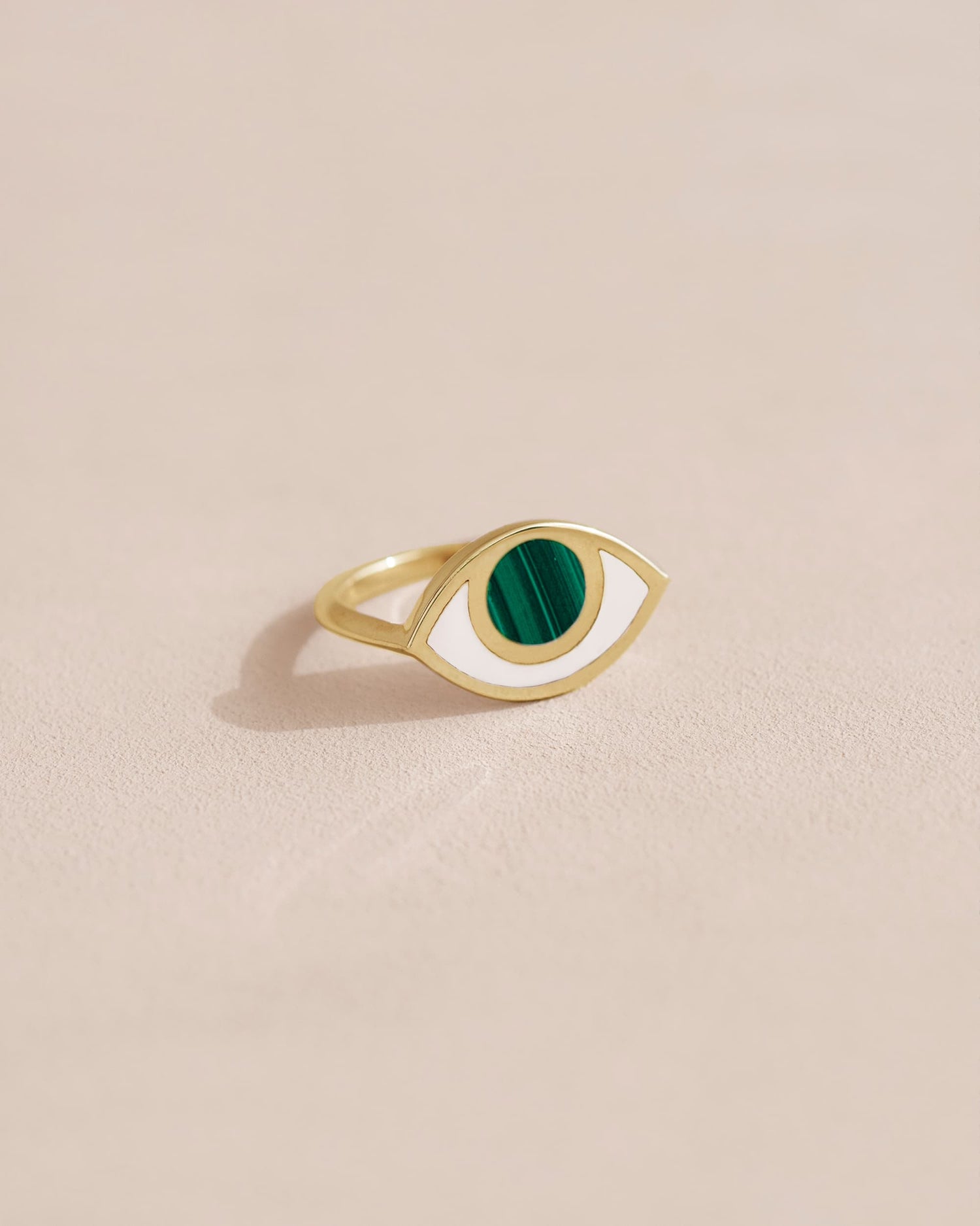 A 14K yellow gold ring with a malachite stone shaped like an eye, placed on a light background.