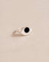 A silver ring with an onyx eye talisman design placed on a beige background.
