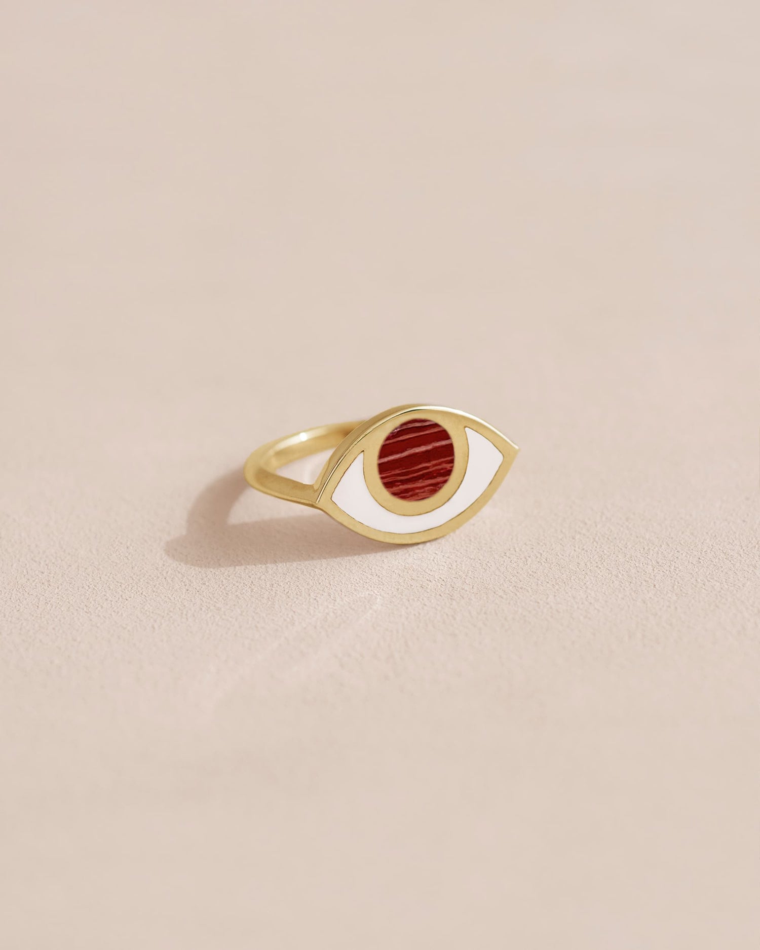 A gold ring with a jasper stone shaped like an eye set in the center, on a plain background.