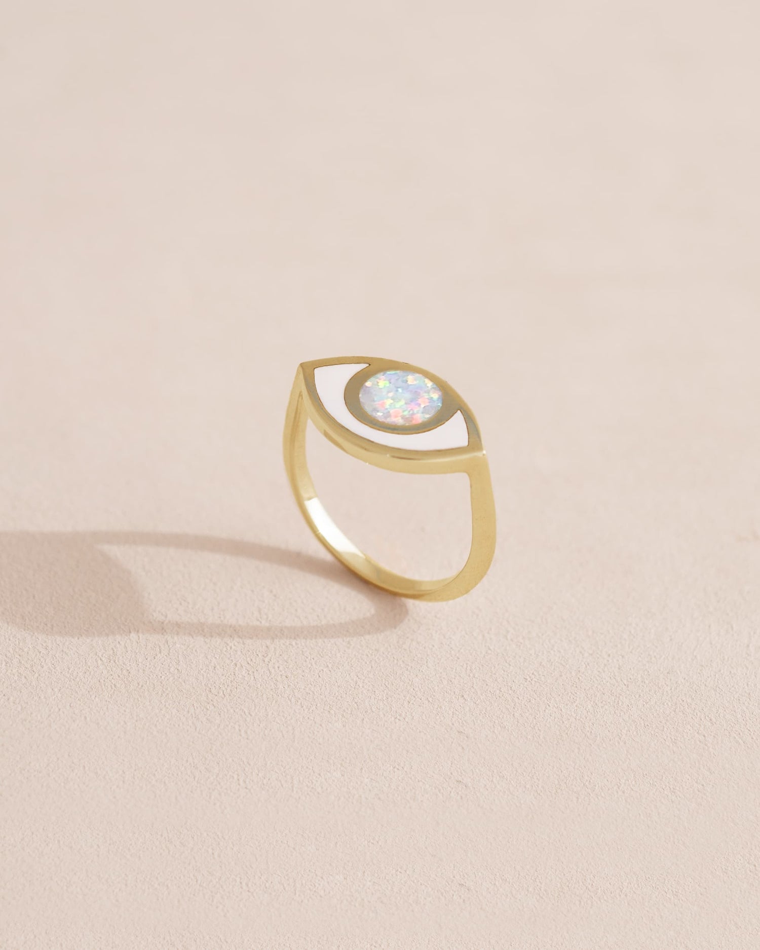 Gold ring with a white opal stone on a light beige background.