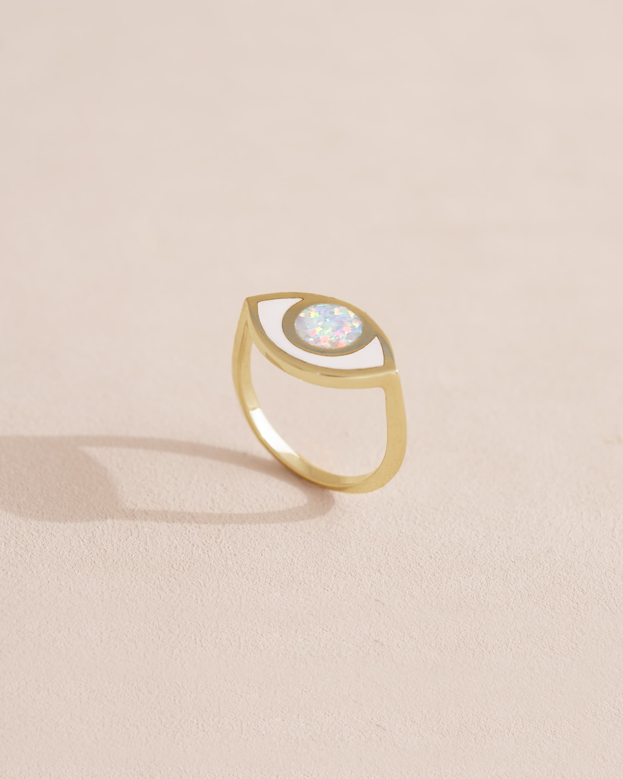Gold ring with a white opal stone on a light beige background.