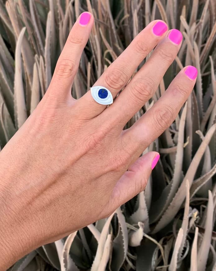 a hand wearing an eye shaped silver ring in front of some agave plants