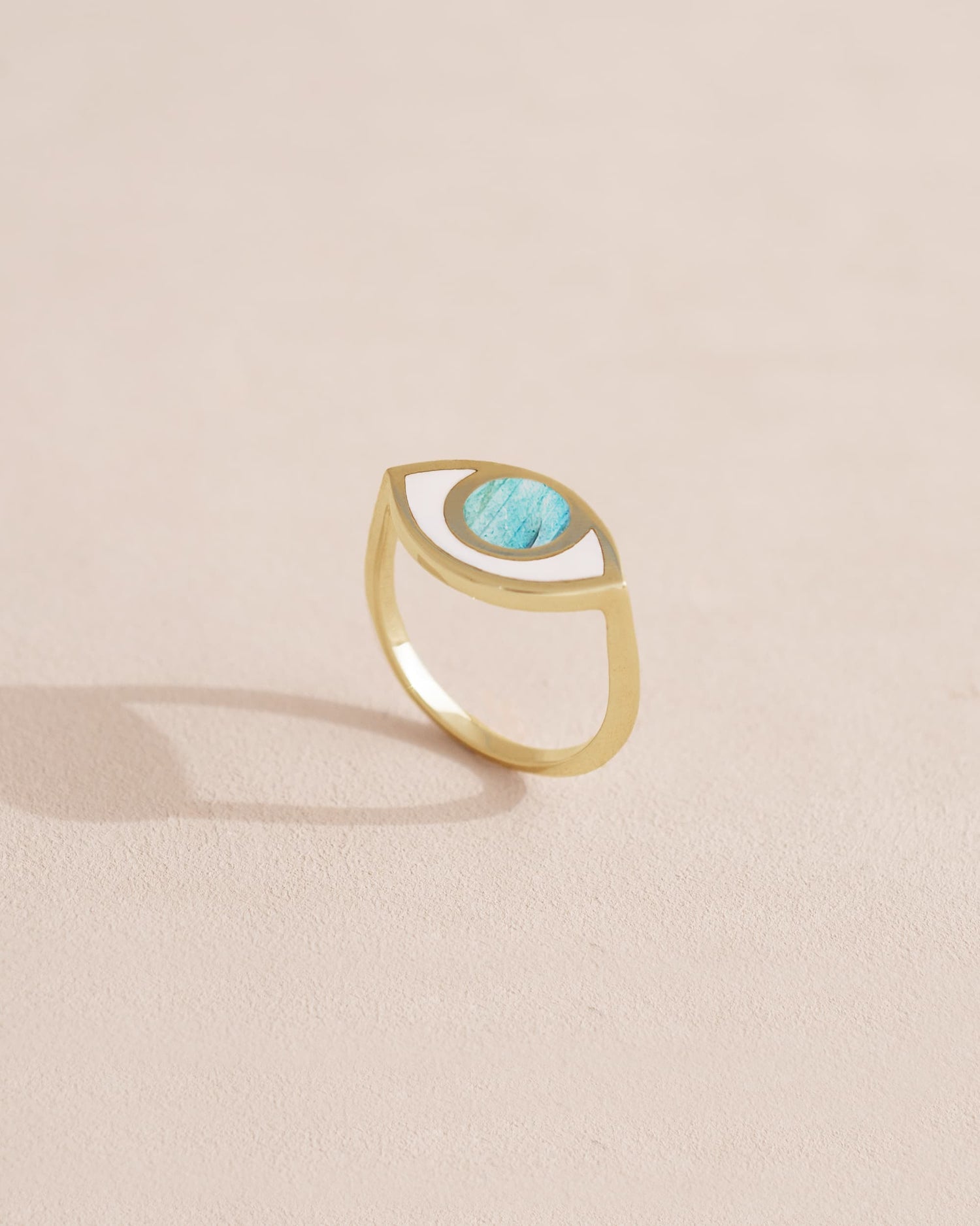 A gold ring featuring a labradorite stone set in a simple setting, resembling an eye, on a light background.