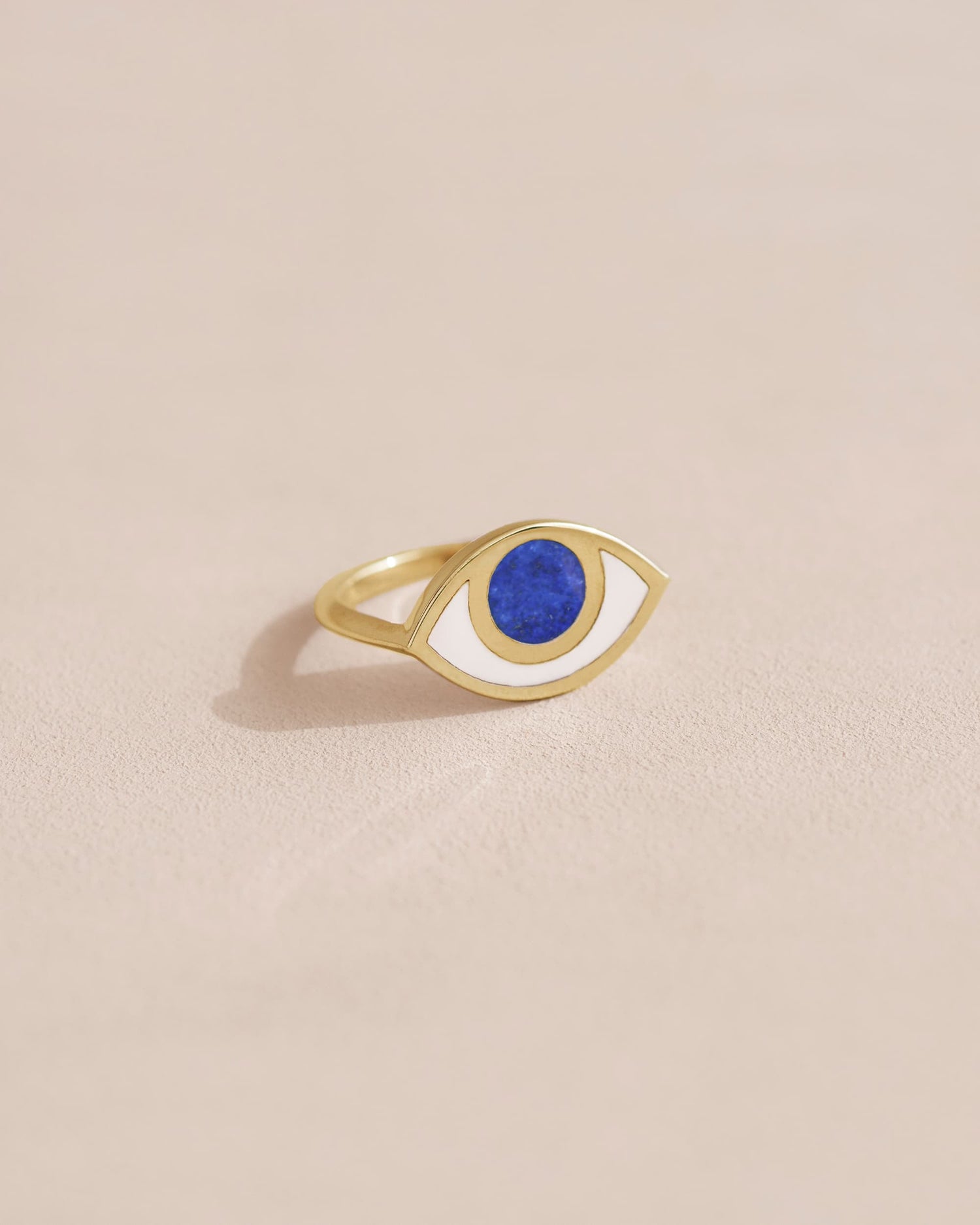 A lapis lazuli ring with a gold band, designed to resemble an eye, placed on a light background.