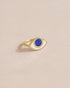 A lapis lazuli ring with a gold band, designed to resemble an eye, placed on a light background.