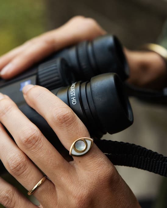 An eye shaped ring worn by a hand holding a pair of binoculars