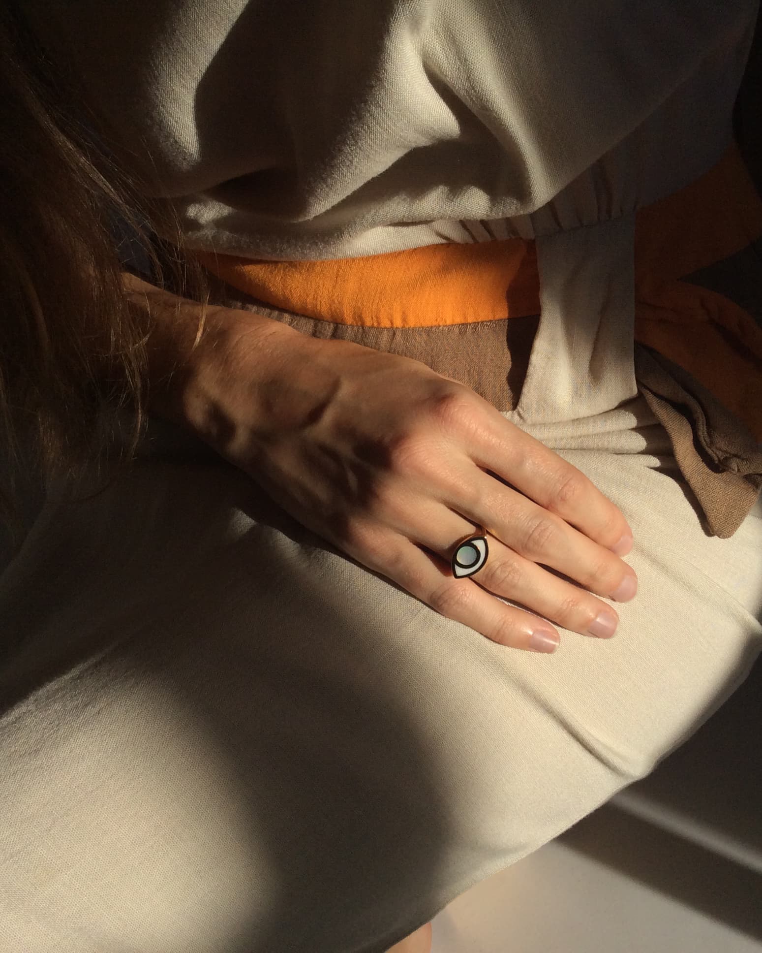 An eye shaped ring worn by a hand gently laying on models lap