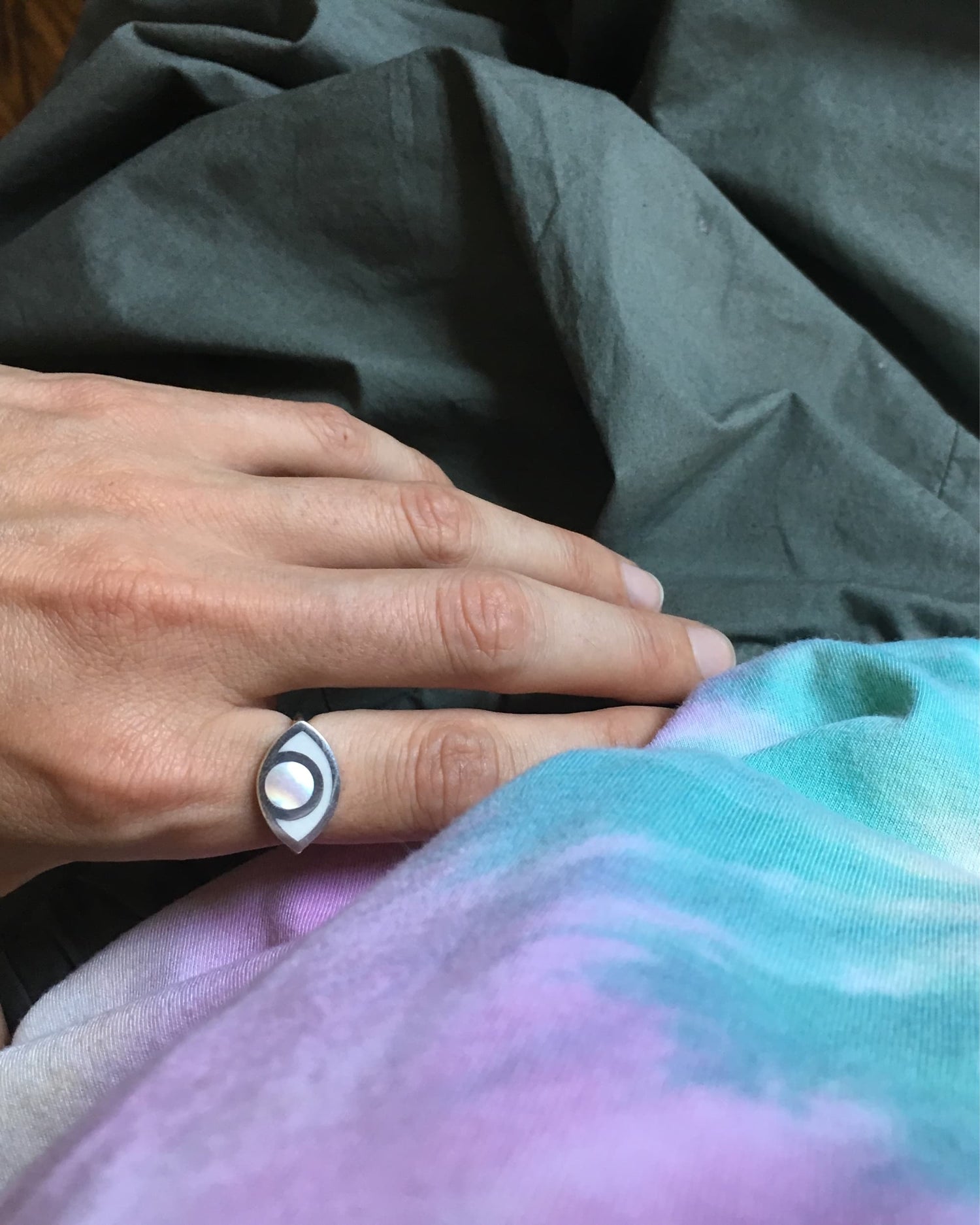 An eye shaped ring worn by a hand against some textiles