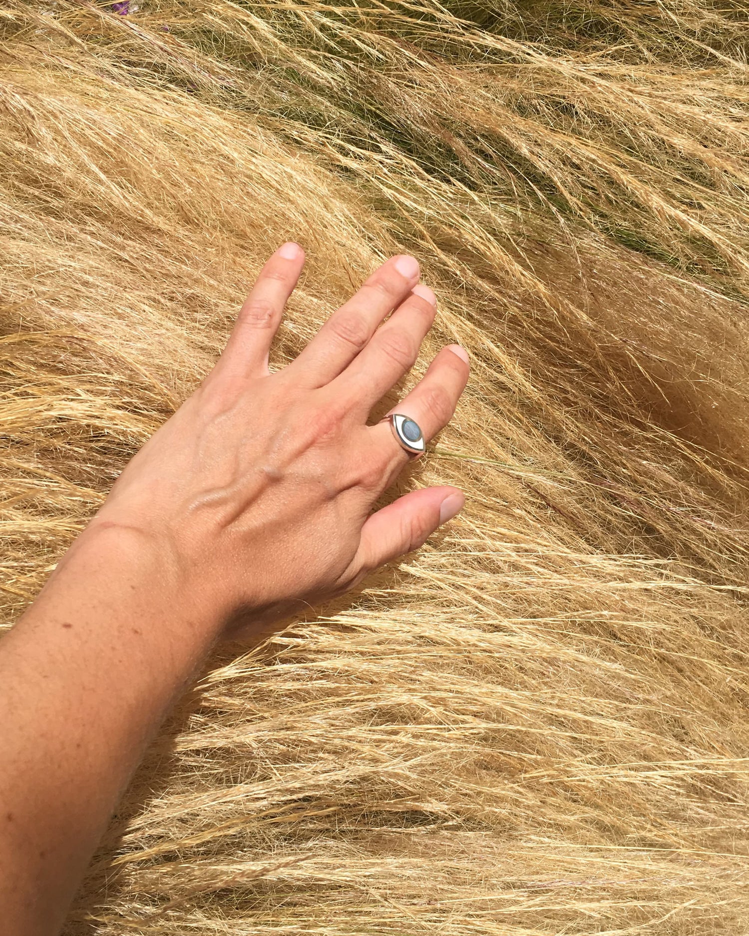 A hand wearing an eye shaped silver ring against some dry hay