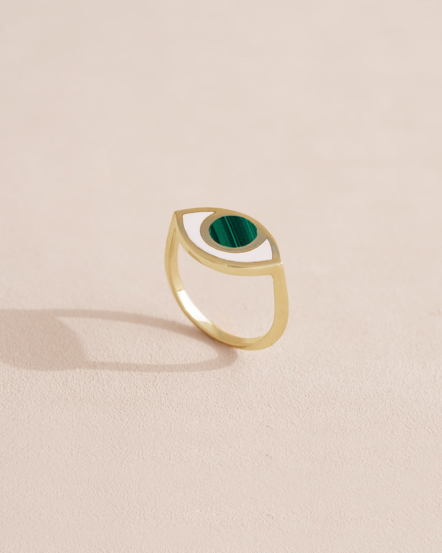 A 14K yellow gold ring with a malachite stone shaped like an eye, placed on a neutral background.