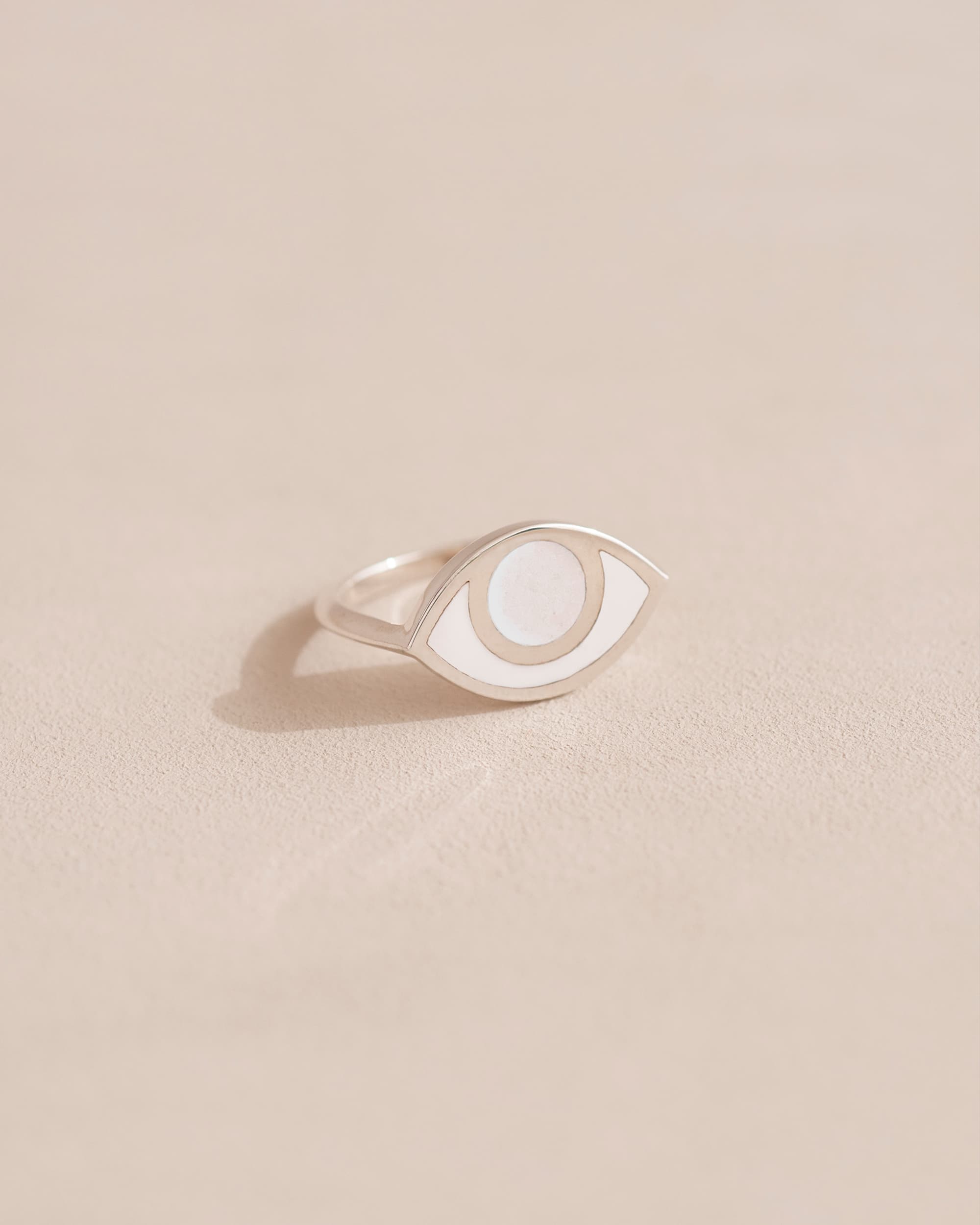 A silver-colored ring with a porcelain eye design on a beige background.