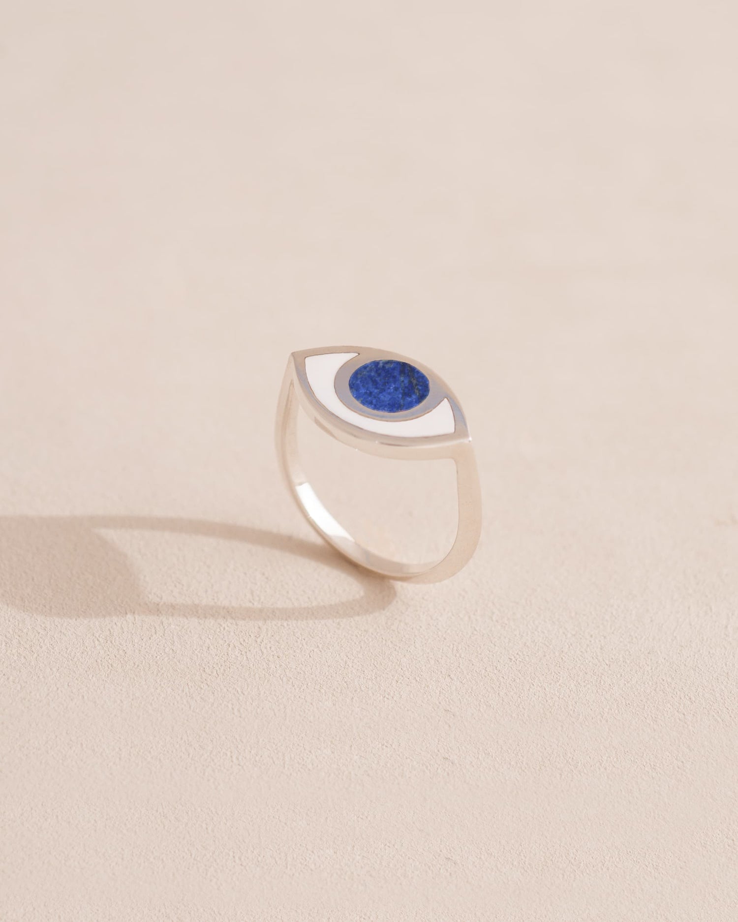 A silver ring shaped like an eye with a lapis lazuli stone set in the center, on a neutral background.