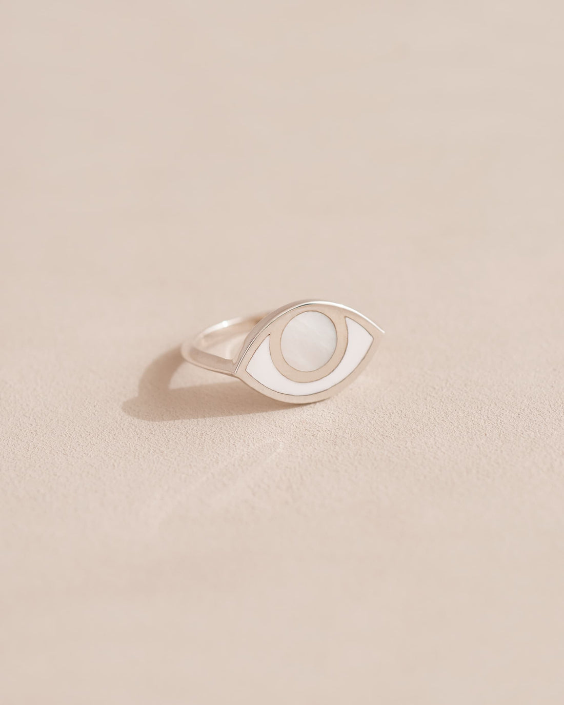 A silver ring shaped like an eye with a mother of pearl stone set in the center, on a neutral background.
