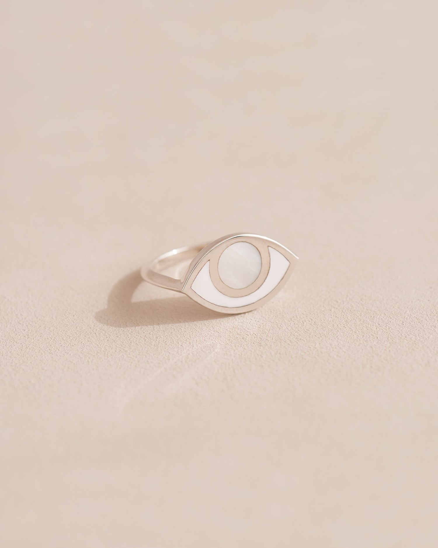 A silver ring shaped like an eye with a mother of pearl stone set in the center, on a neutral background.