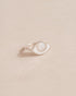 A silver ring shaped like an eye with a mother of pearl stone set in the center, on a neutral background.