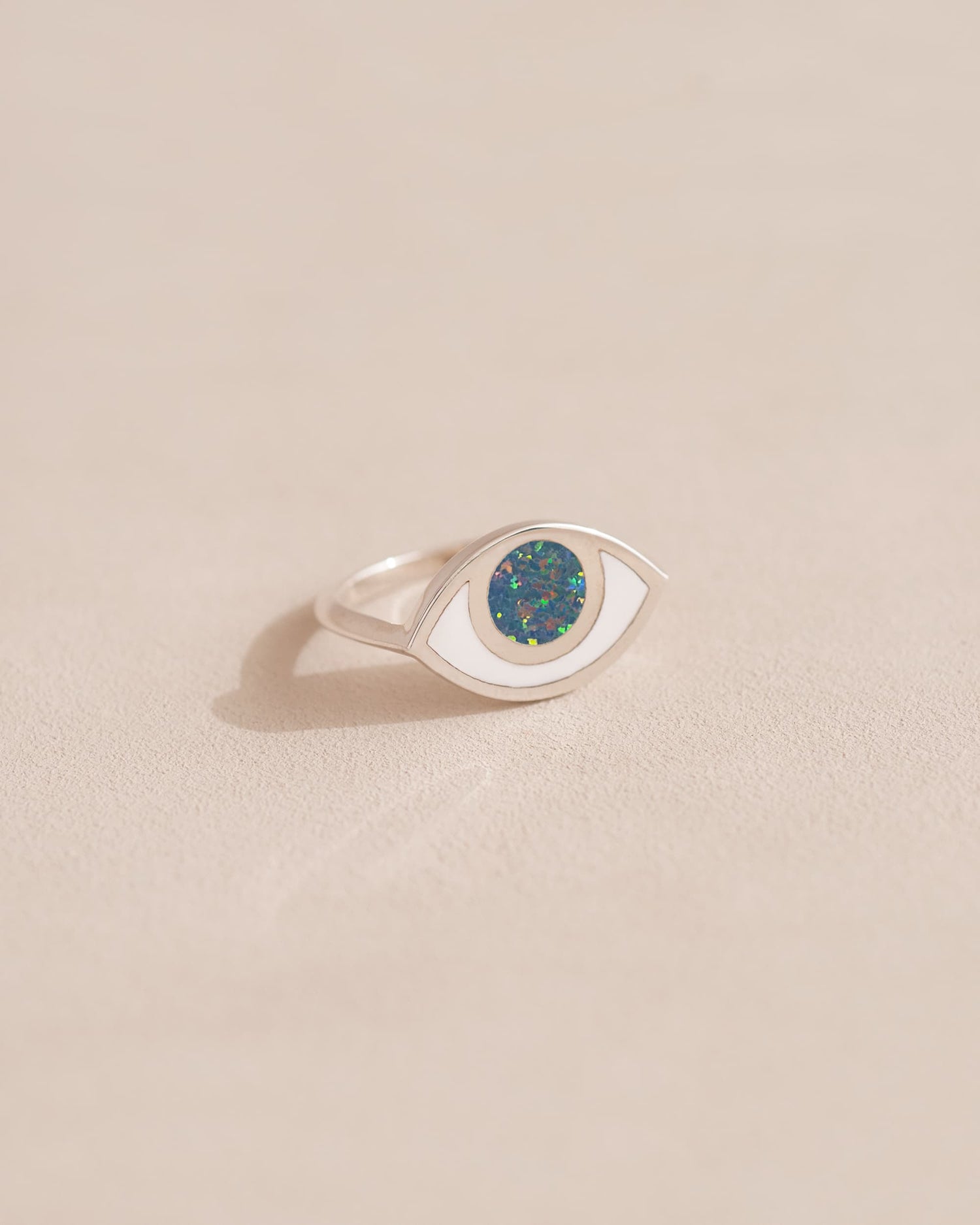 A silver ring shaped like an eye with a dark opal stone set in the center, on a neutral background.