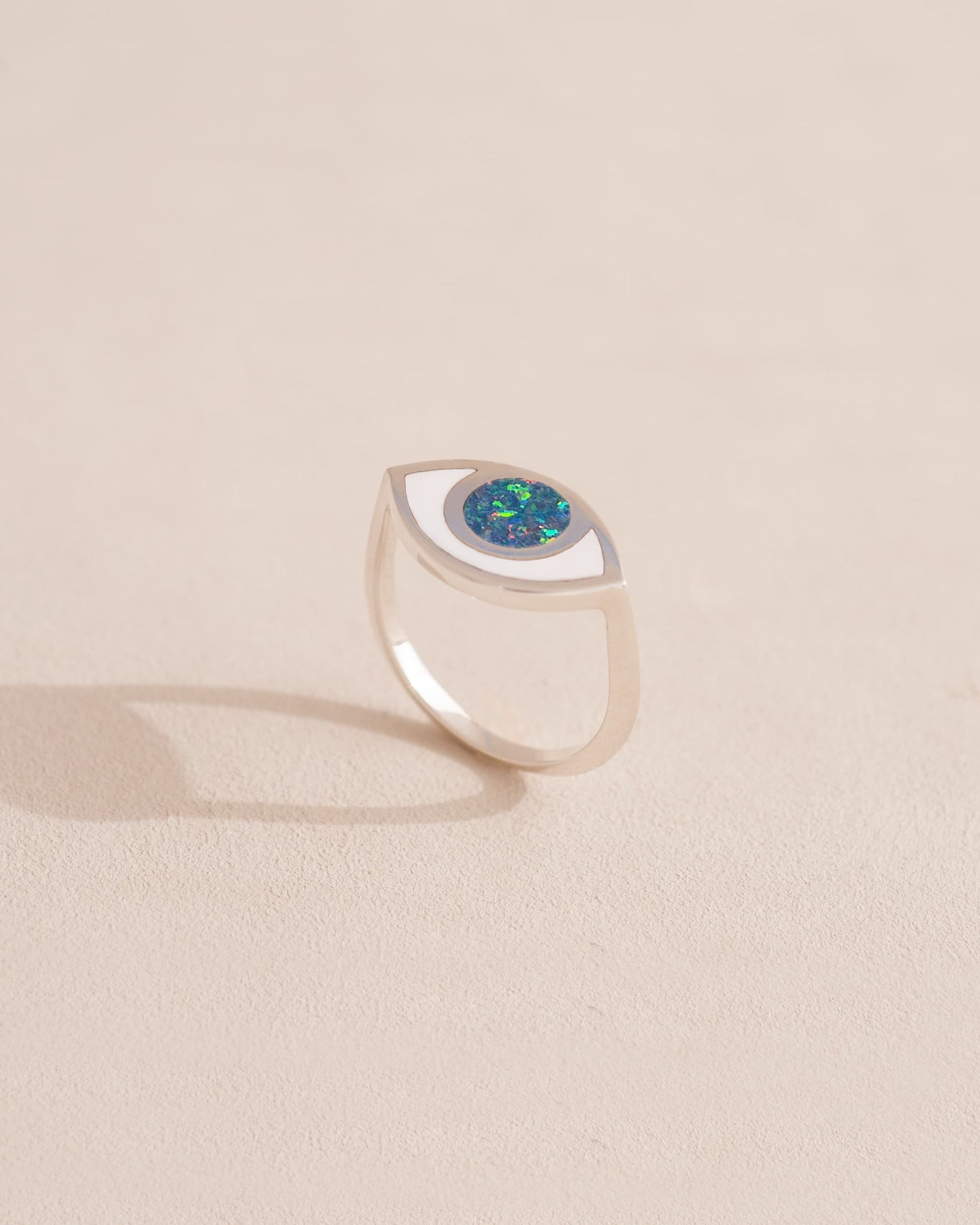 A silver ring shaped like an eye with a starry opal stone set in the center, on a neutral background.