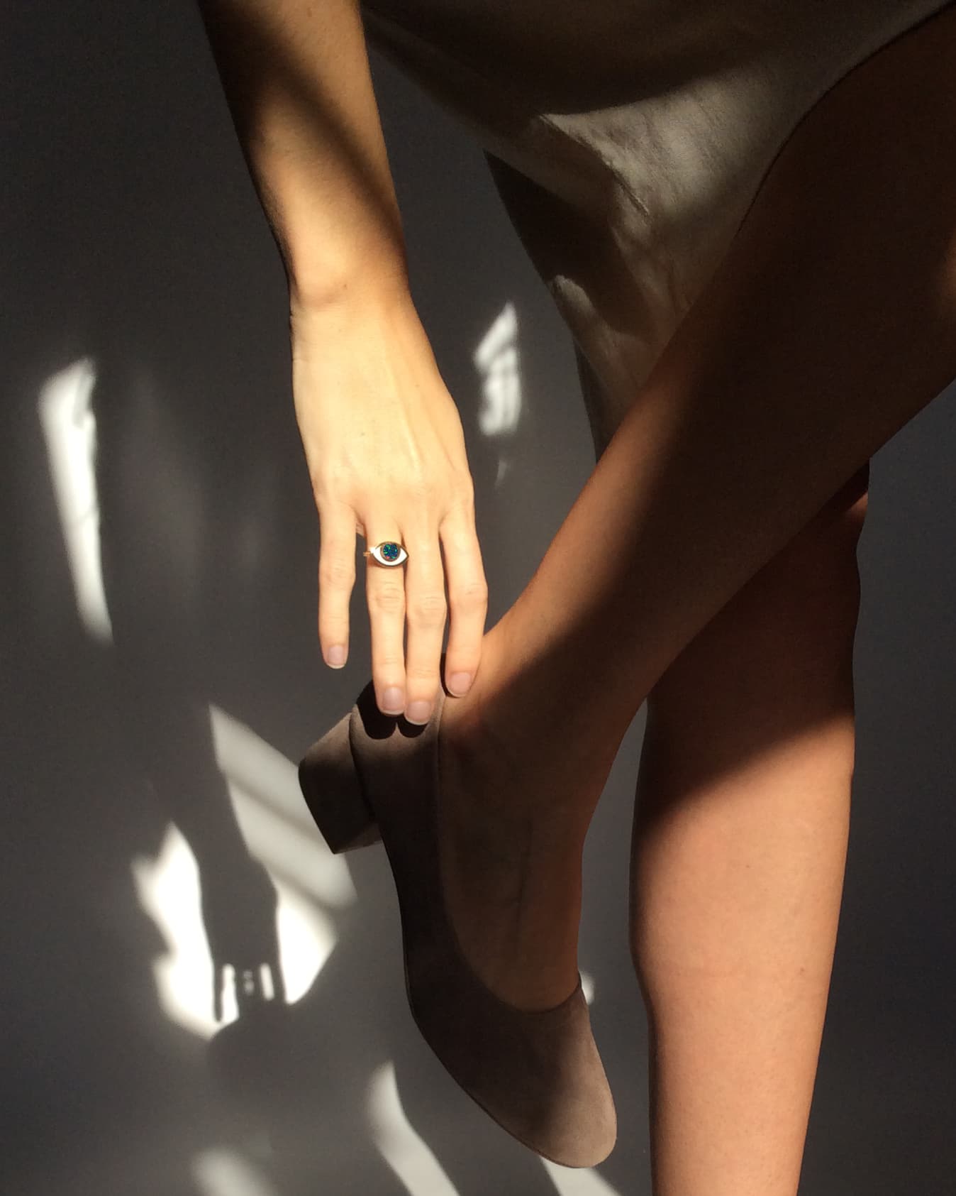 An eye shaped ring worn by a hand holding touching a shoe