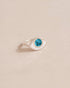 A silver ring with a turquoise stone shaped like an eye, placed on a neutral background.