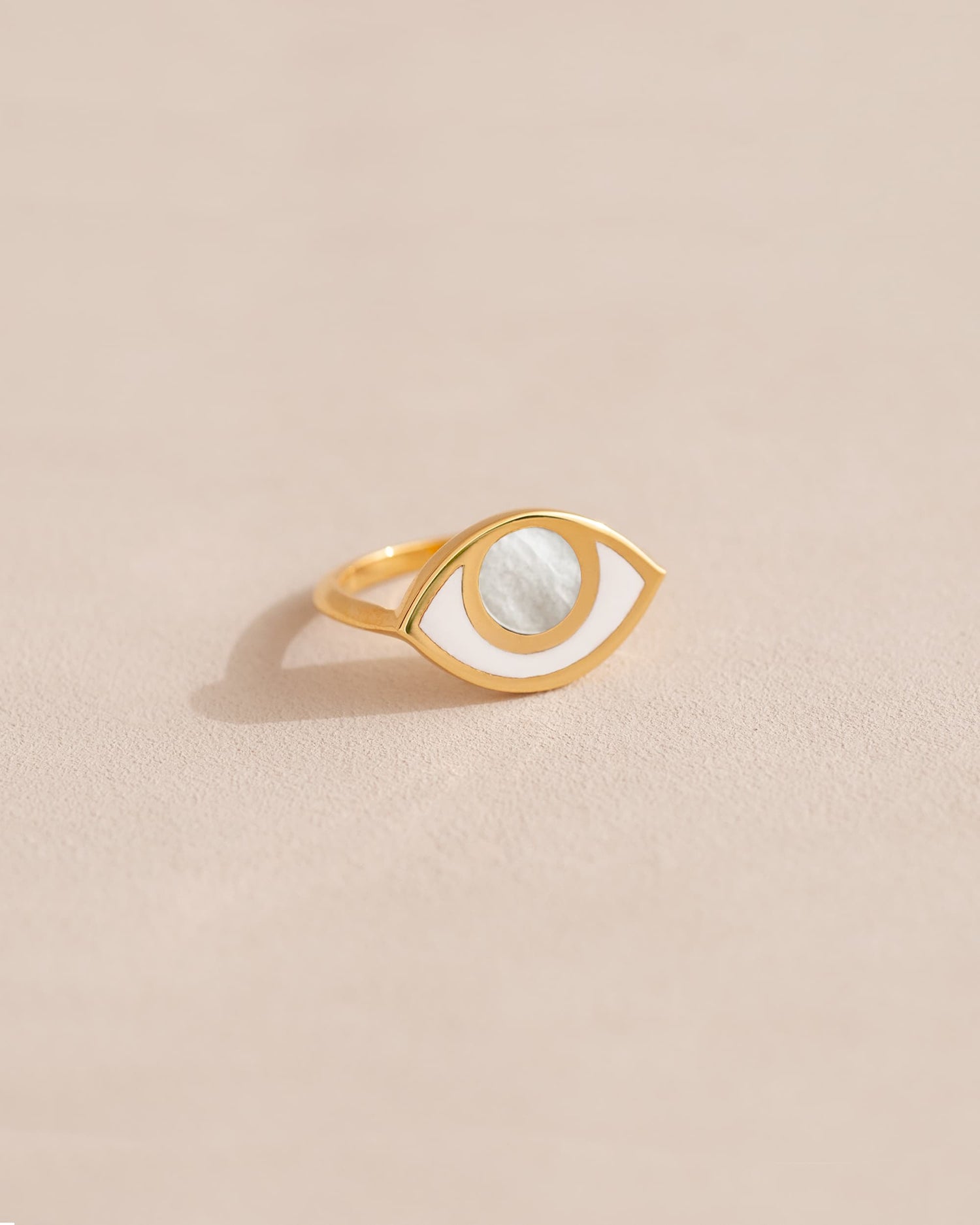 a gold ring shaped like an eye featuring a round mother of pearl center
