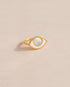 a gold ring shaped like an eye featuring a round mother of pearl center