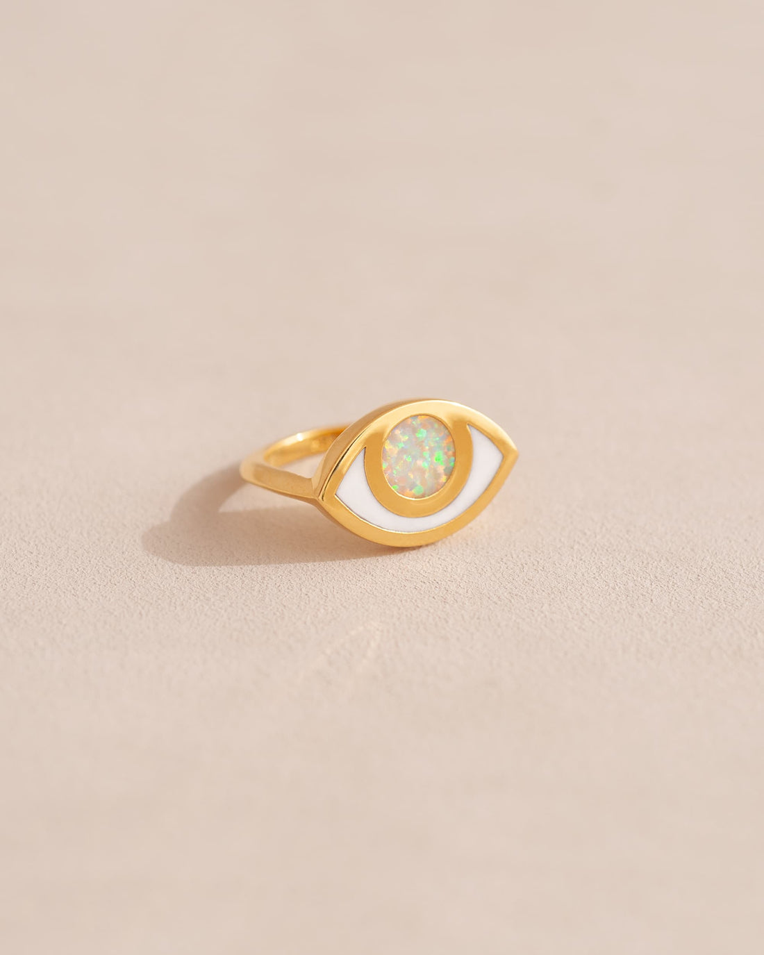 A gold ring shaped like an eye with an opal stone set in the center, on a neutral background.