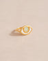 A gold ring shaped like an eye with an opal stone set in the center, on a neutral background.