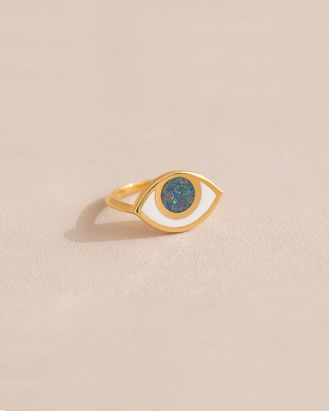 A gold ring shaped like an eye with a starry opal stone set in the center, on a neutral background.