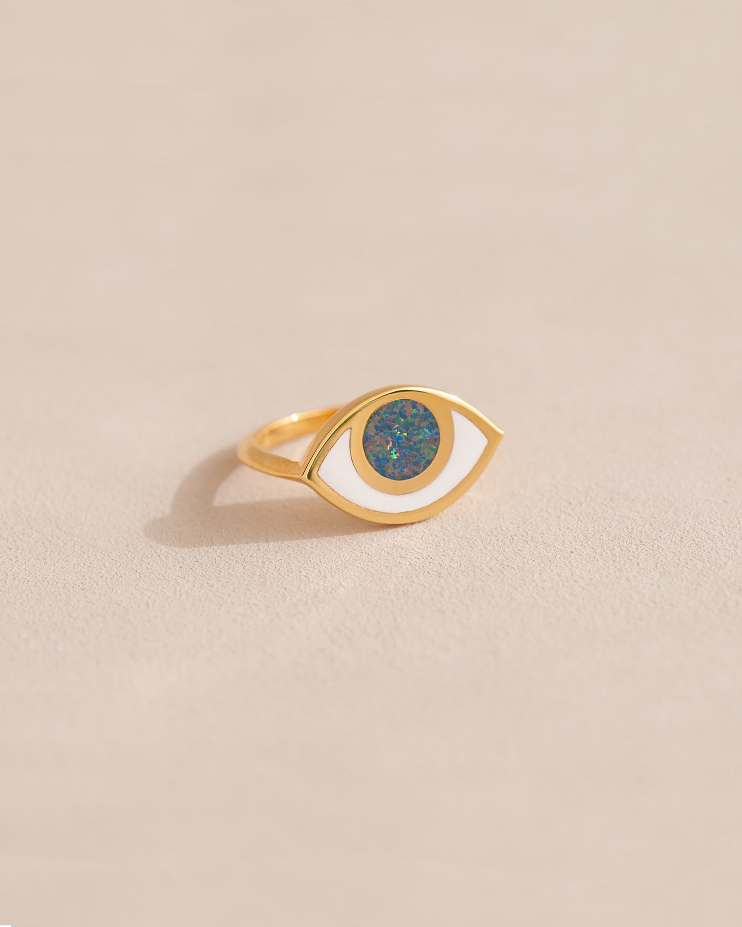 A gold ring shaped like an eye with a starry opal stone set in the center, on a neutral background.